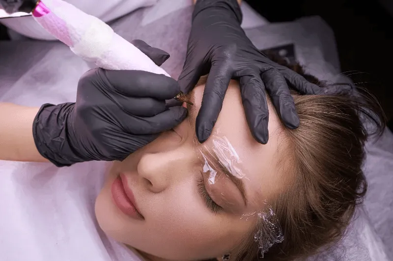 The image shows a person undergoing an eyebrow tattoo procedure, highlighting the importance of careful post-procedure care and maintenance to ensure optimal results and healing.
