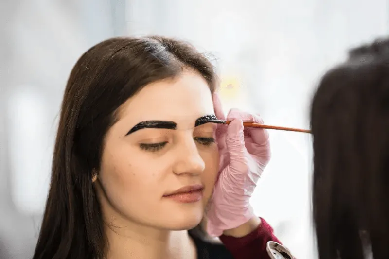 The image shows a professional applying eyebrow pigment during a tattooing process